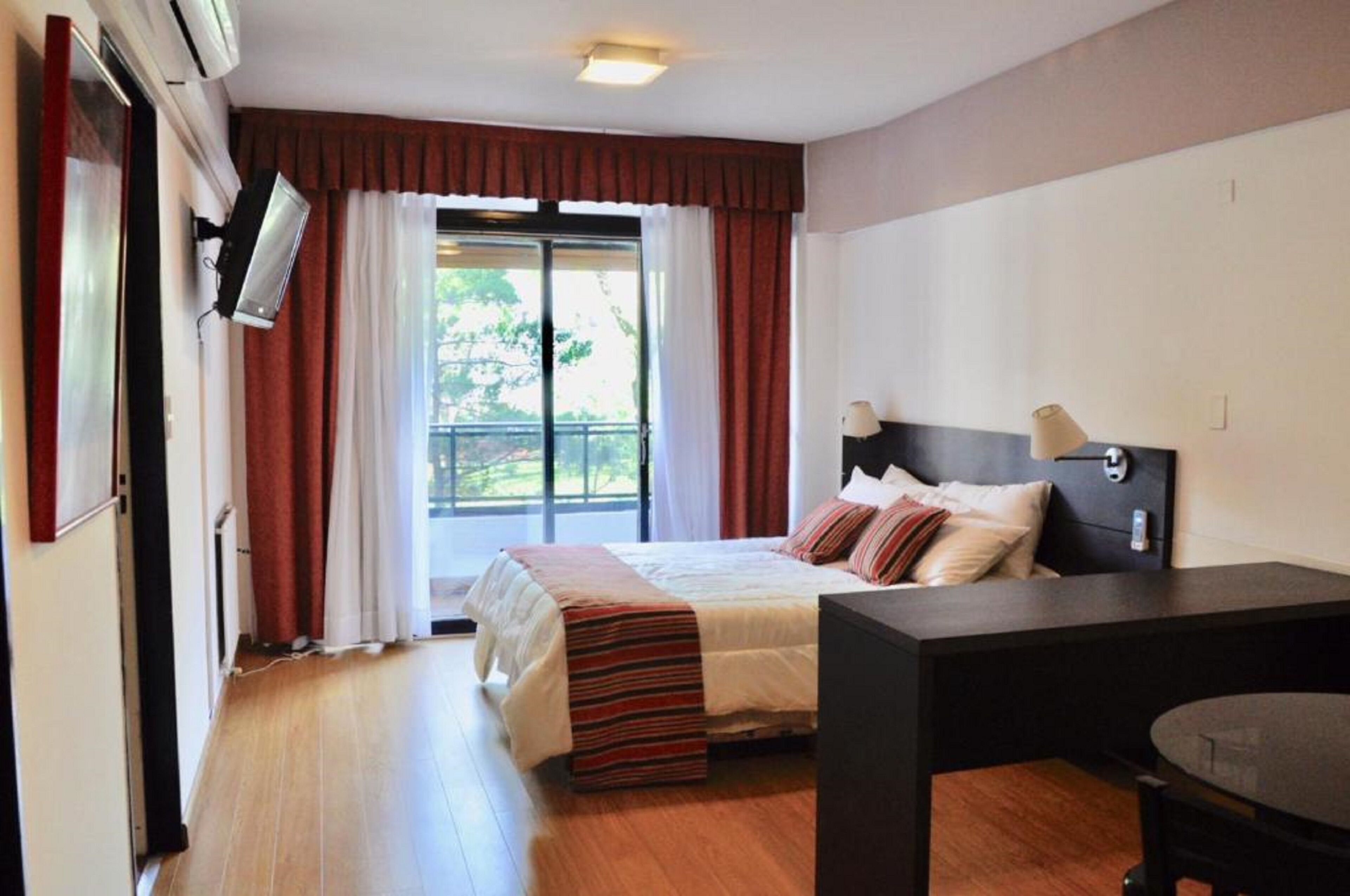 Een hotelkamer met een bed, een bureau, een stoel, een televisie en een balkon met gordijnen.