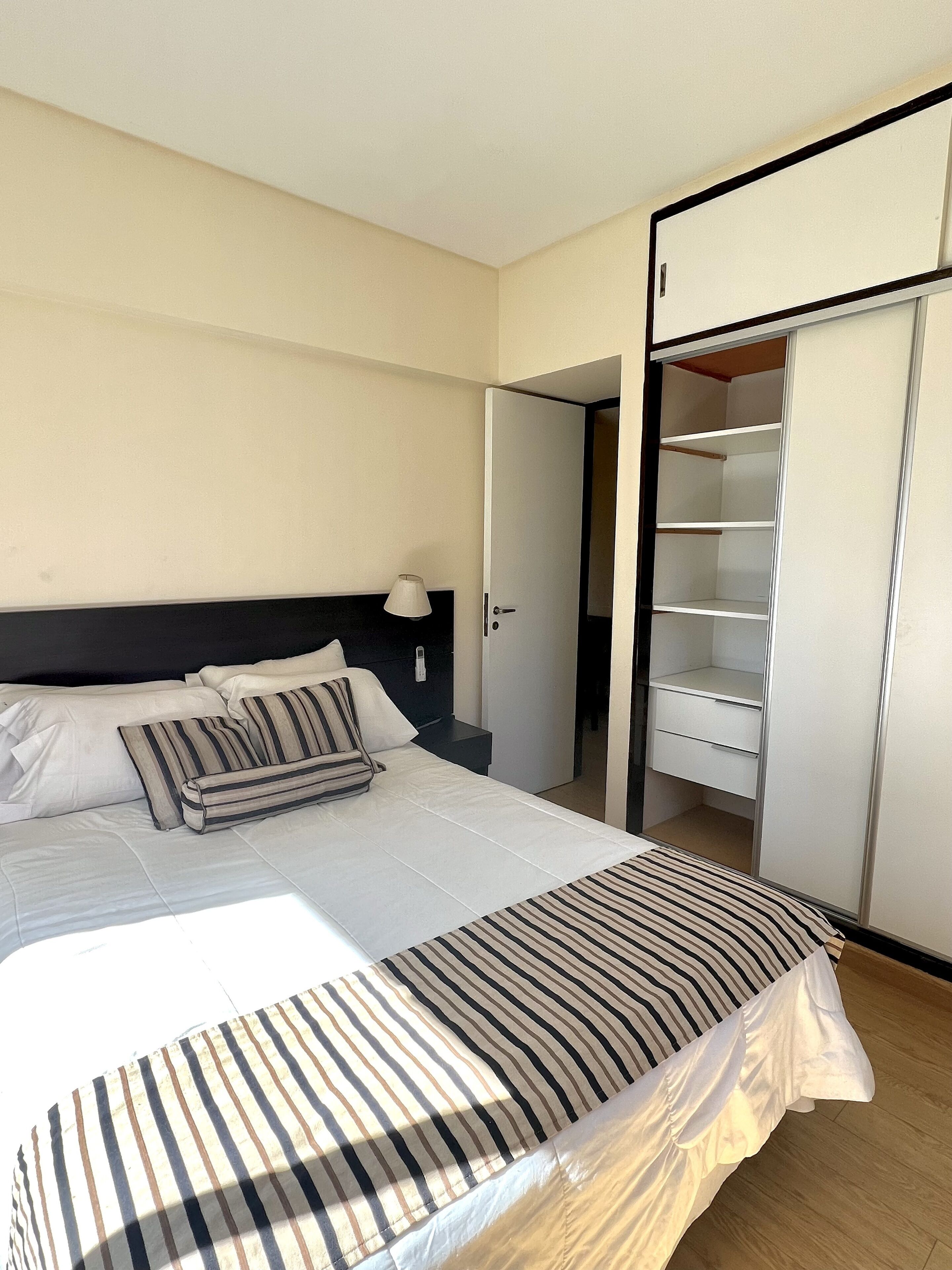 Habitación de hotel con cama, mesita de noche, lámpara y armario.