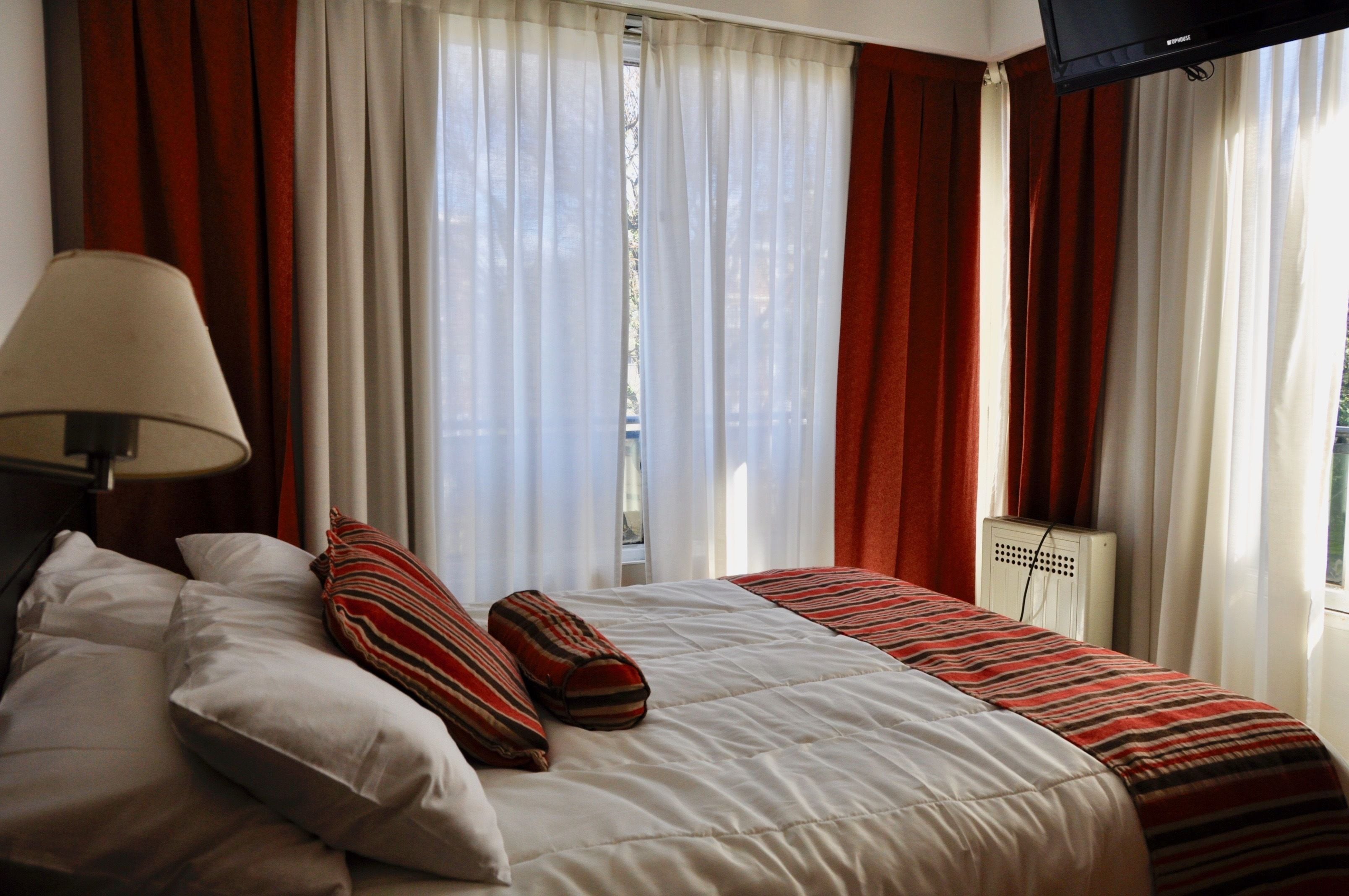 Et hotelværelse med seng, puder, lampe og gardiner.