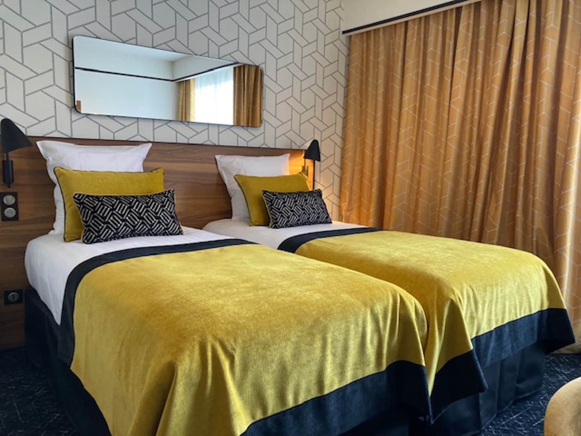 A hotel room with two beds, a mirror, a clock, and a patterned wall.