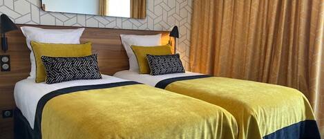 A hotel room with two beds, a mirror, a clock, and a patterned wall.
