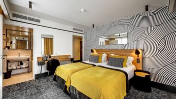 Una habitación de hotel con una cama, un tocador con espejo, un escritorio y un papel tapiz estampado.