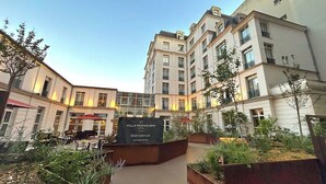 A courtyard with outdoor seating, a sign for Villa Modigliani Hotel, and a building with multiple balconies. - Hôtel Vacances Bleues Villa Modigliani (Paris)