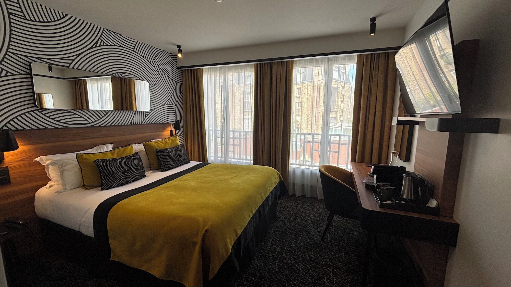 Een hotelkamer met een bed, een bureau, een stoel, een televisie en een raam met gordijnen.