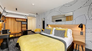 A modern hotel room with a bed, a desk, a chair, a wardrobe, and a mirror.