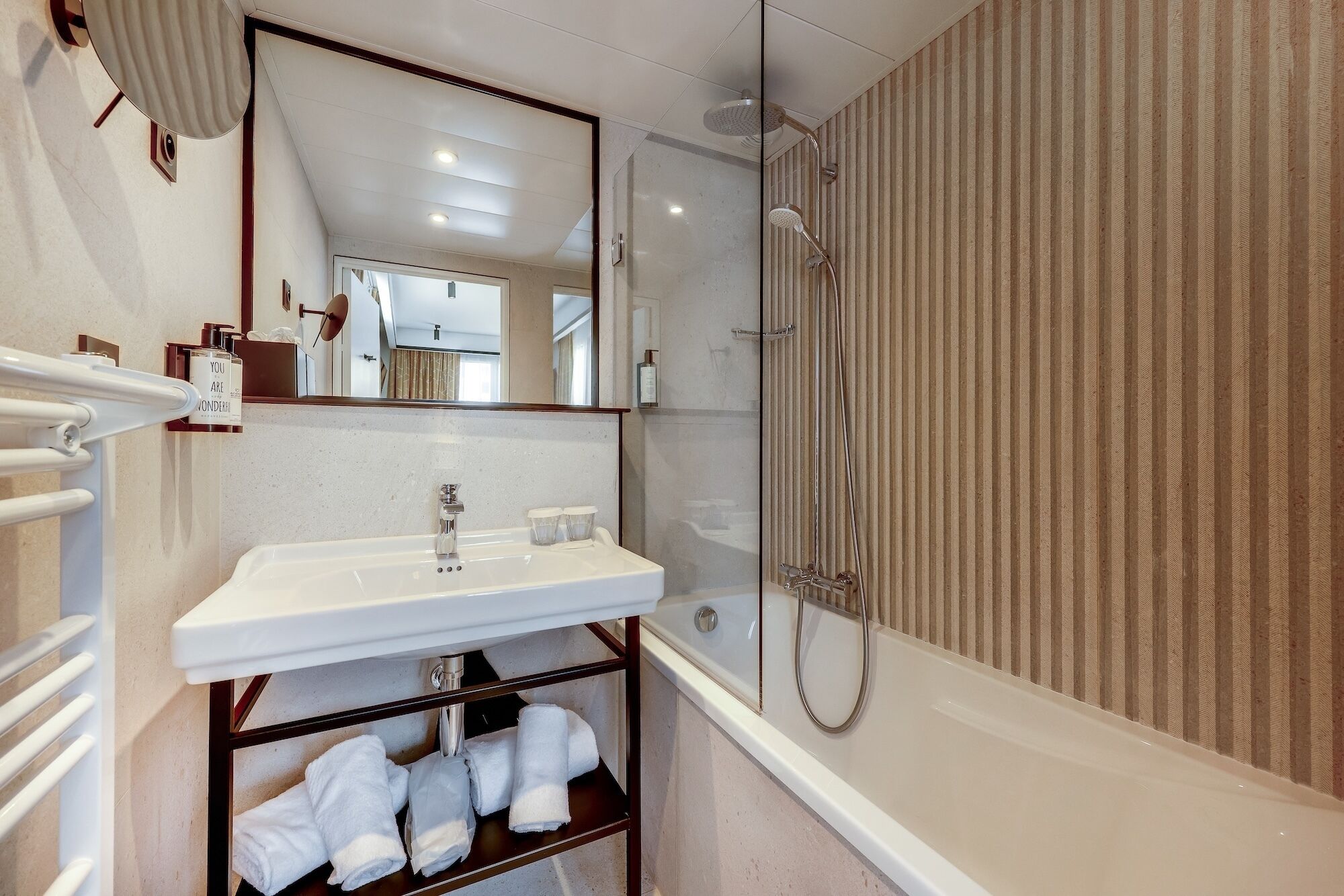 Une salle de bain avec un lavabo blanc, un miroir, une douche et un porte-serviettes avec des serviettes.
