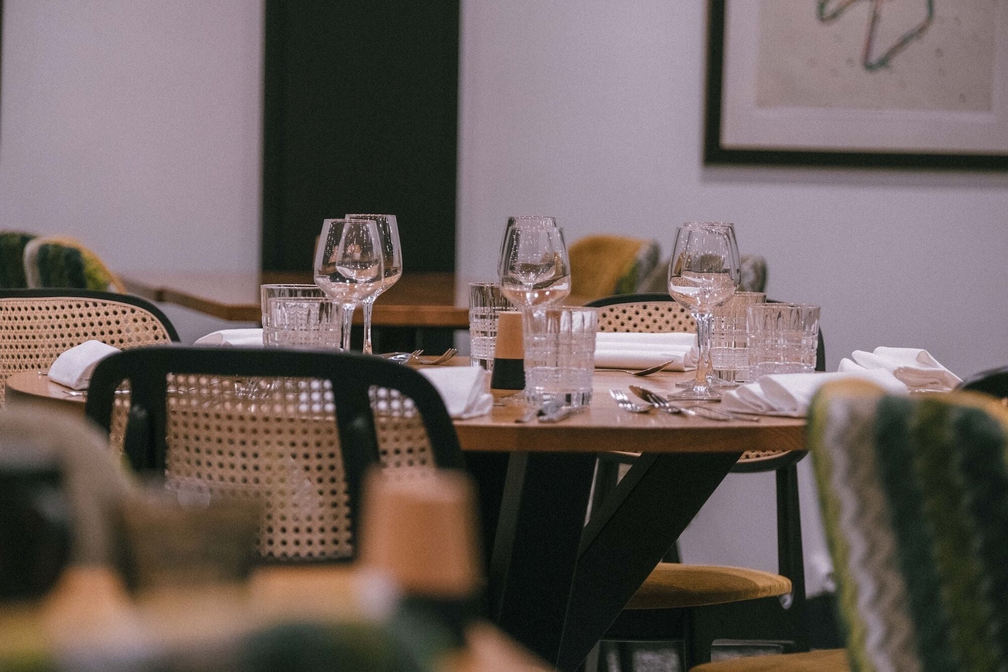 A dining table set with glasses, cutlery, and a napkin, surrounded by wicker chairs.