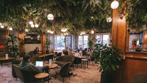 A modern indoor space with seating, tables, and hanging plants. - Hôtel Vacances Bleues Villa Modigliani (Paris)