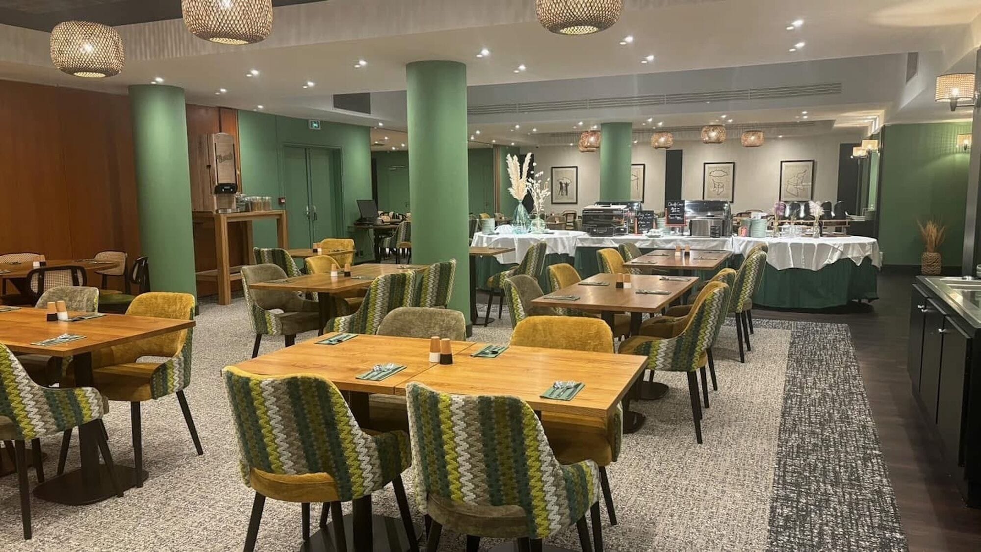 Zona de menjador d'hotel amb diverses taules i cadires, un sistema de buffet i parets verdes.