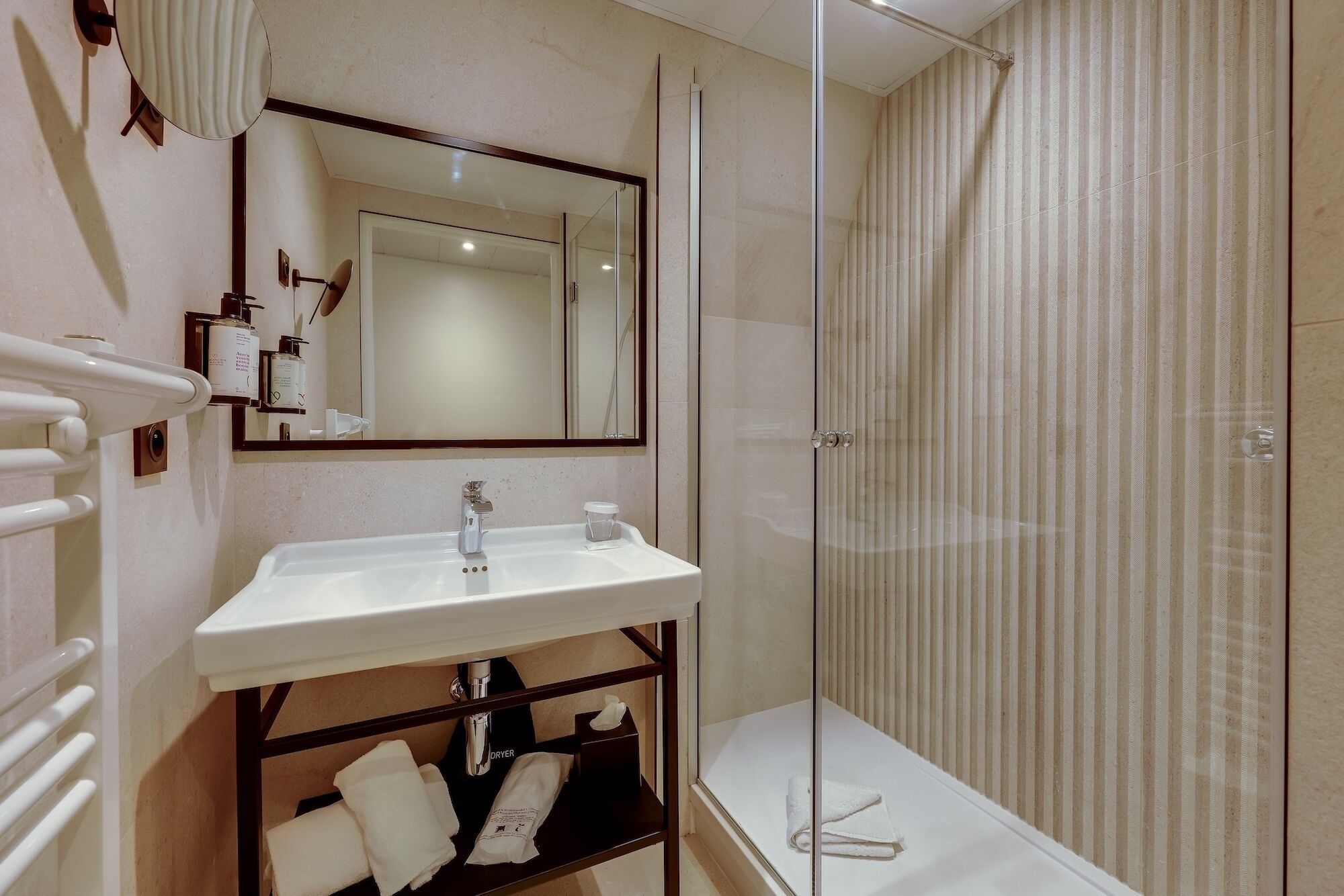 Une salle de bain avec un lavabo blanc, un miroir, un porte-serviettes et une cabine de douche en verre.