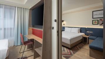 A hotel room with a bed, a desk, a chair, a sofa, and a TV.