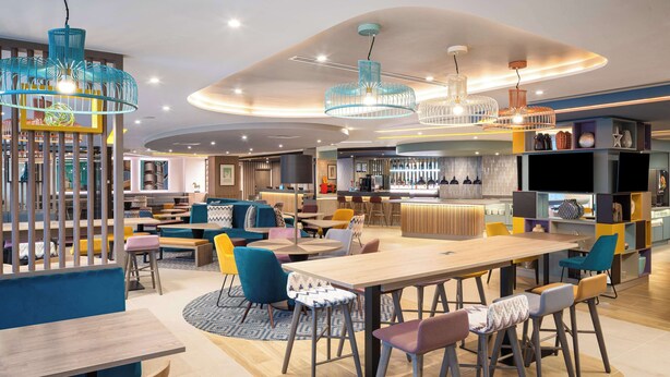 A modern interior with a central dining area, bar, and seating arrangements. - Hampton by Hilton London City (London)
