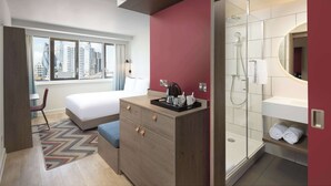 A modern hotel room with a bed, a desk, a chair, a dresser, a shower, and a city view. - Hampton by Hilton London City (London)