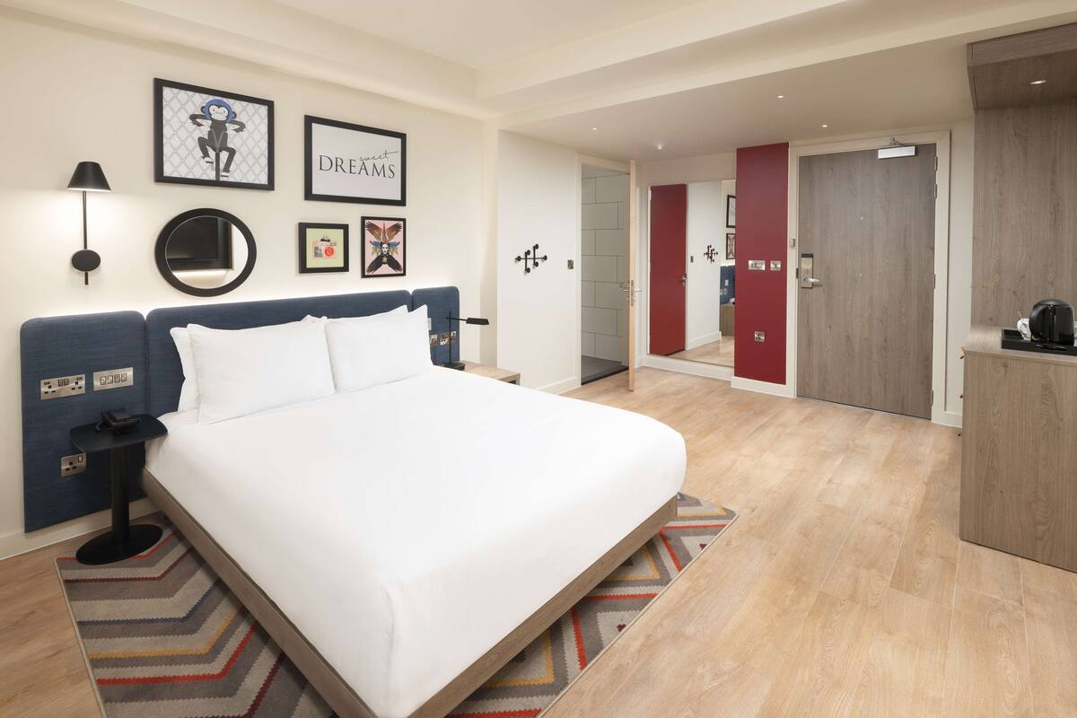 A modern hotel room with a large bed, a desk, and a wardrobe.