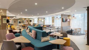 A modern lounge area with a teal sofa, multiple seating options, and a variety of tables and chairs. - Hampton by Hilton London City (London)