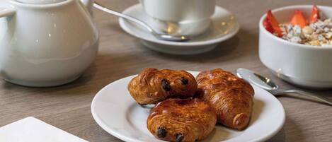 A table with croissants, a teapot, a cup, and a bowl of cereal.