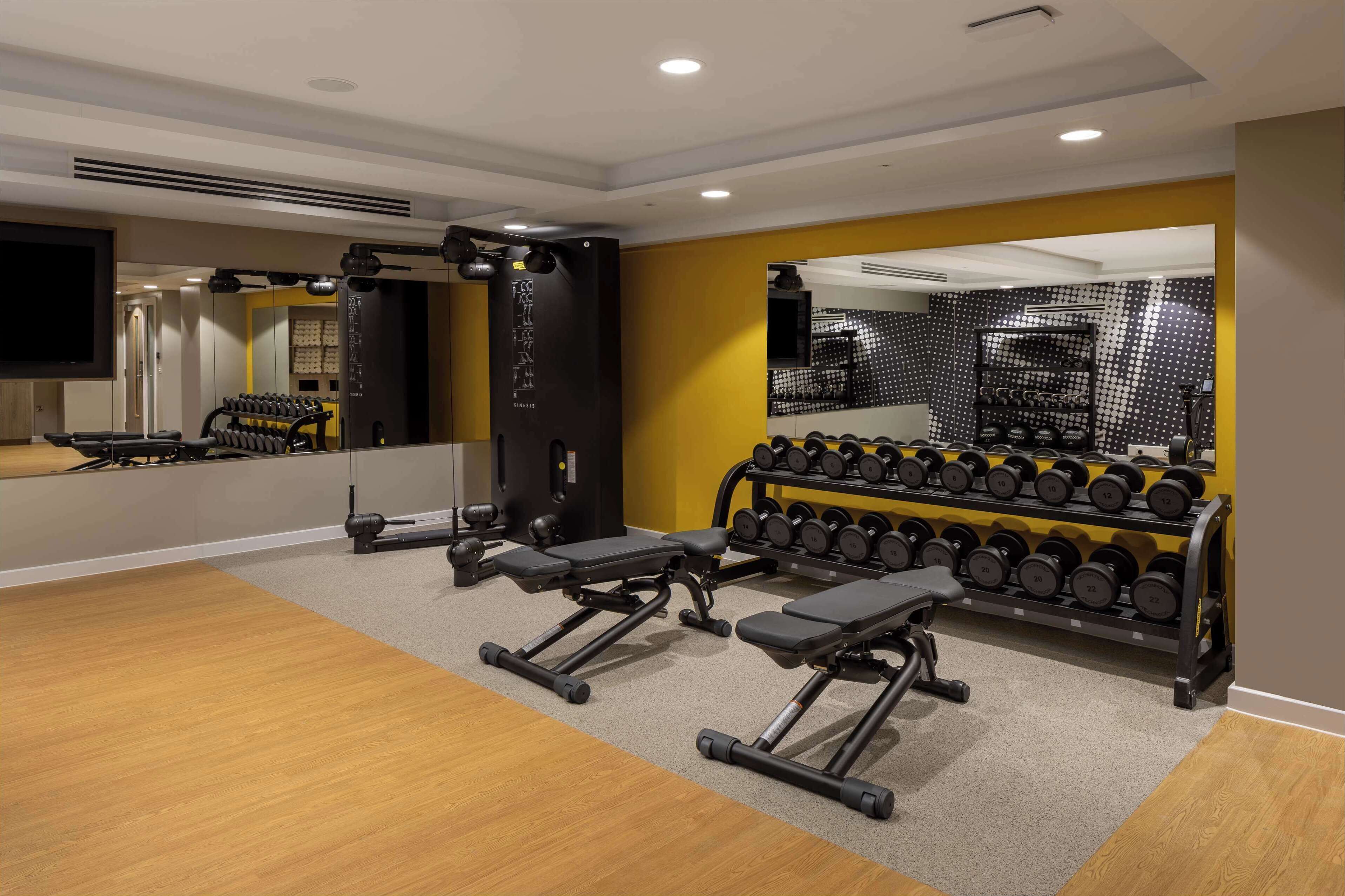 A modern gym with weightlifting equipment, benches, and a mirror.