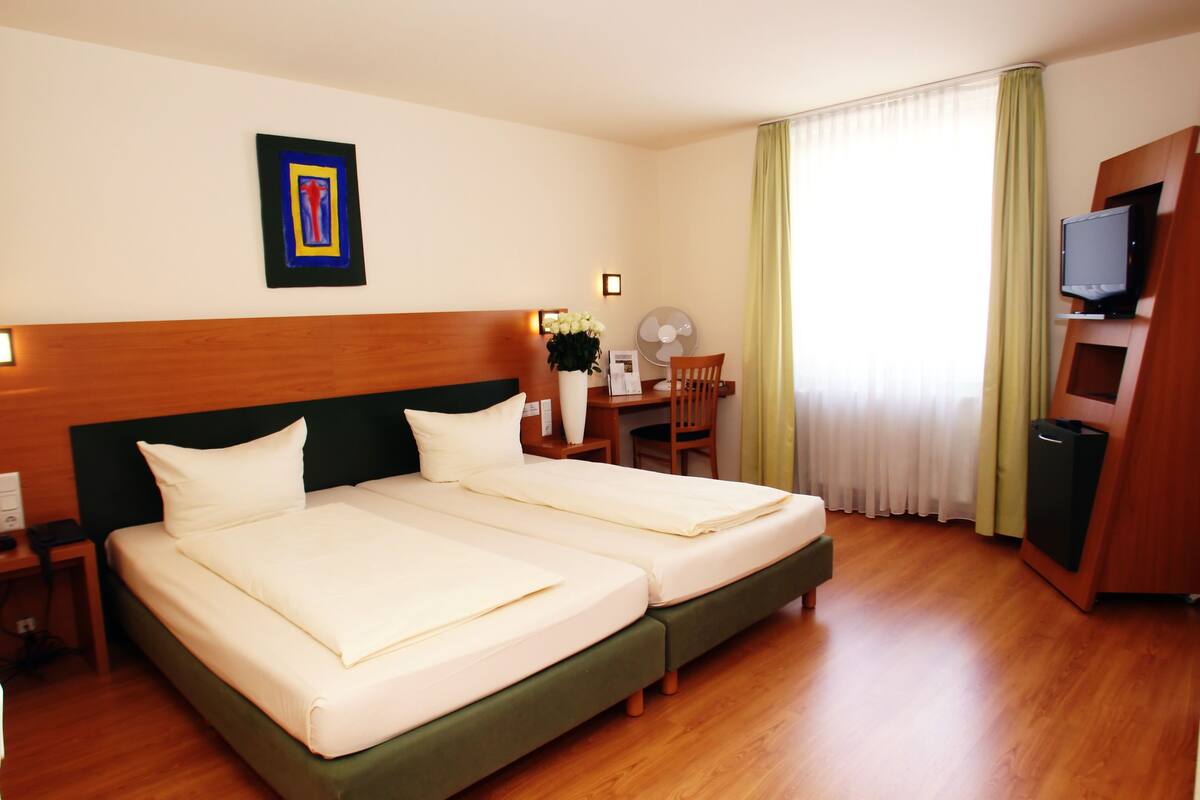 Une chambre d’hôtel avec deux lits, un bureau avec une chaise, une télévision et un ventilateur.
