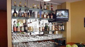 A bar area with shelves of bottles and glasses, a television, and a fruit bowl. - Memphis Hotel (Frankfurt)