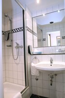 Un bagno con doccia vetrata, un lavandino bianco e uno specchio sopra il lavandino.