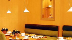 A dining area with a wooden table, green upholstered benches, and pendant lighting. - Memphis Hotel (Frankfurt)