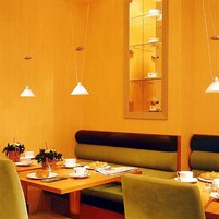 Zona pranzo con tavolo in legno, panche rivestite in verde e lampade a sospensione.