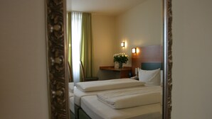 A hotel room with two beds, a nightstand with a lamp, and a mirror. - Memphis Hotel (Frankfurt)