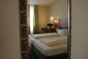 Una camera d'albergo con due letti, un comodino con una lampada e uno specchio.