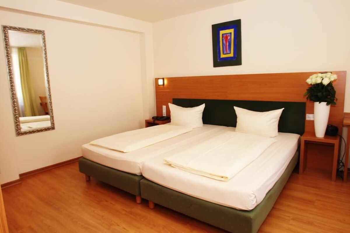 A double bed with a wooden headboard, two bedside tables, a mirror, and a framed artwork on the wall.