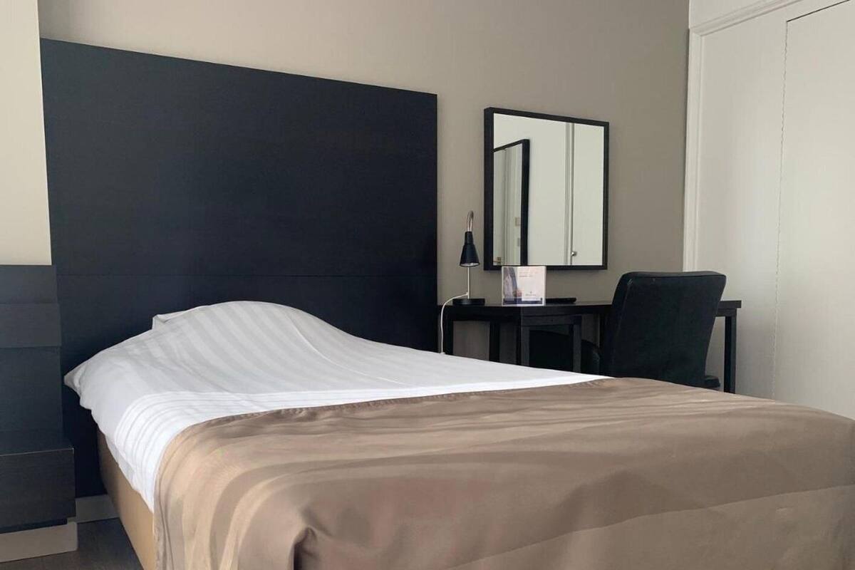 A hotel room with a bed, a desk, a chair, and a mirror.