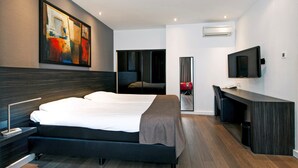 A modern hotel room with a large bed, a desk, a flat-screen TV, and a painting on the wall.