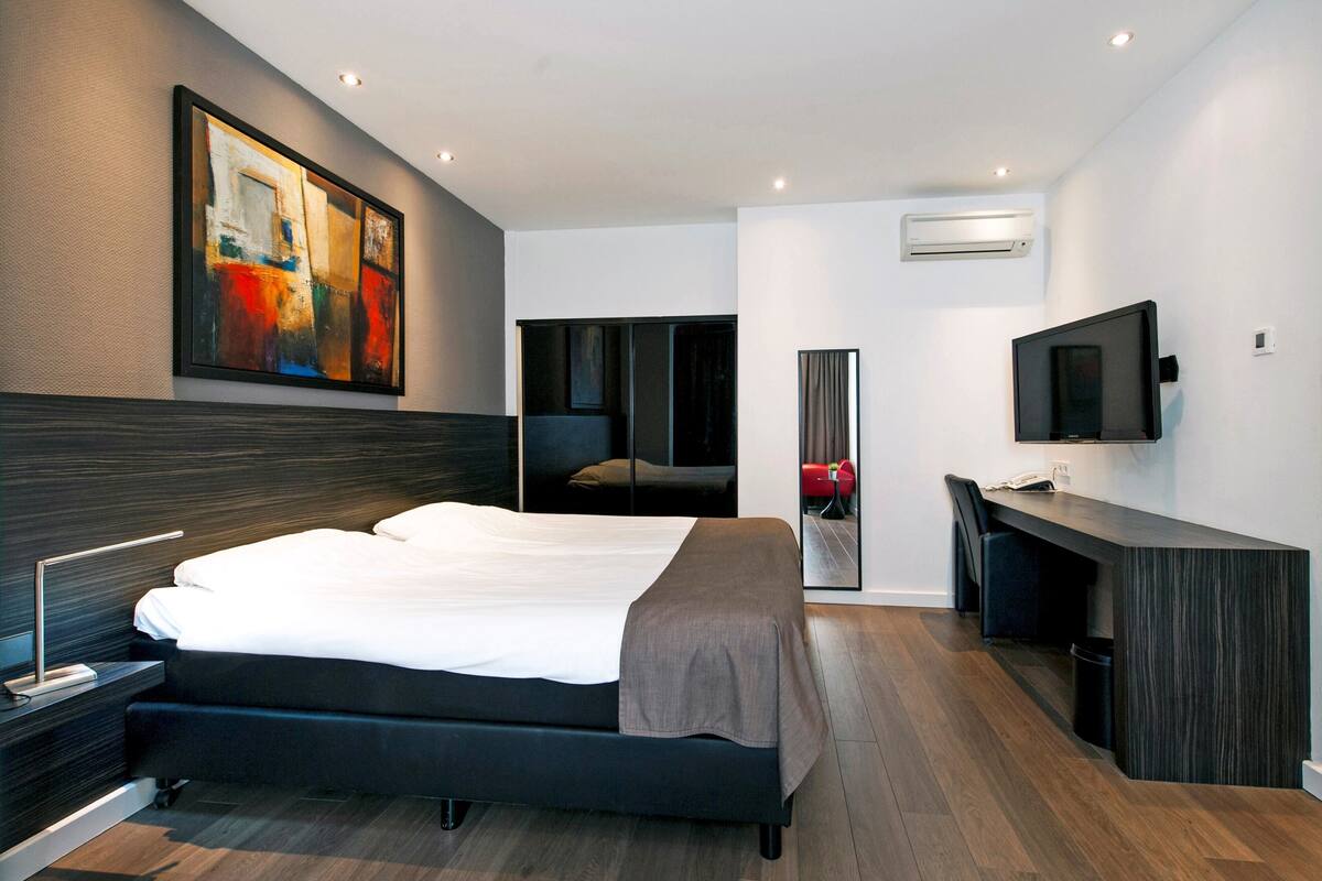A modern hotel room with a large bed, a desk, a flat-screen TV, and a painting on the wall.