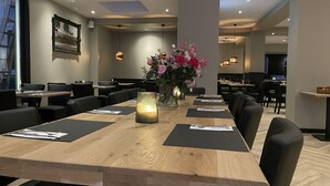A restaurant with a long wooden table, black chairs, and a vase of flowers.