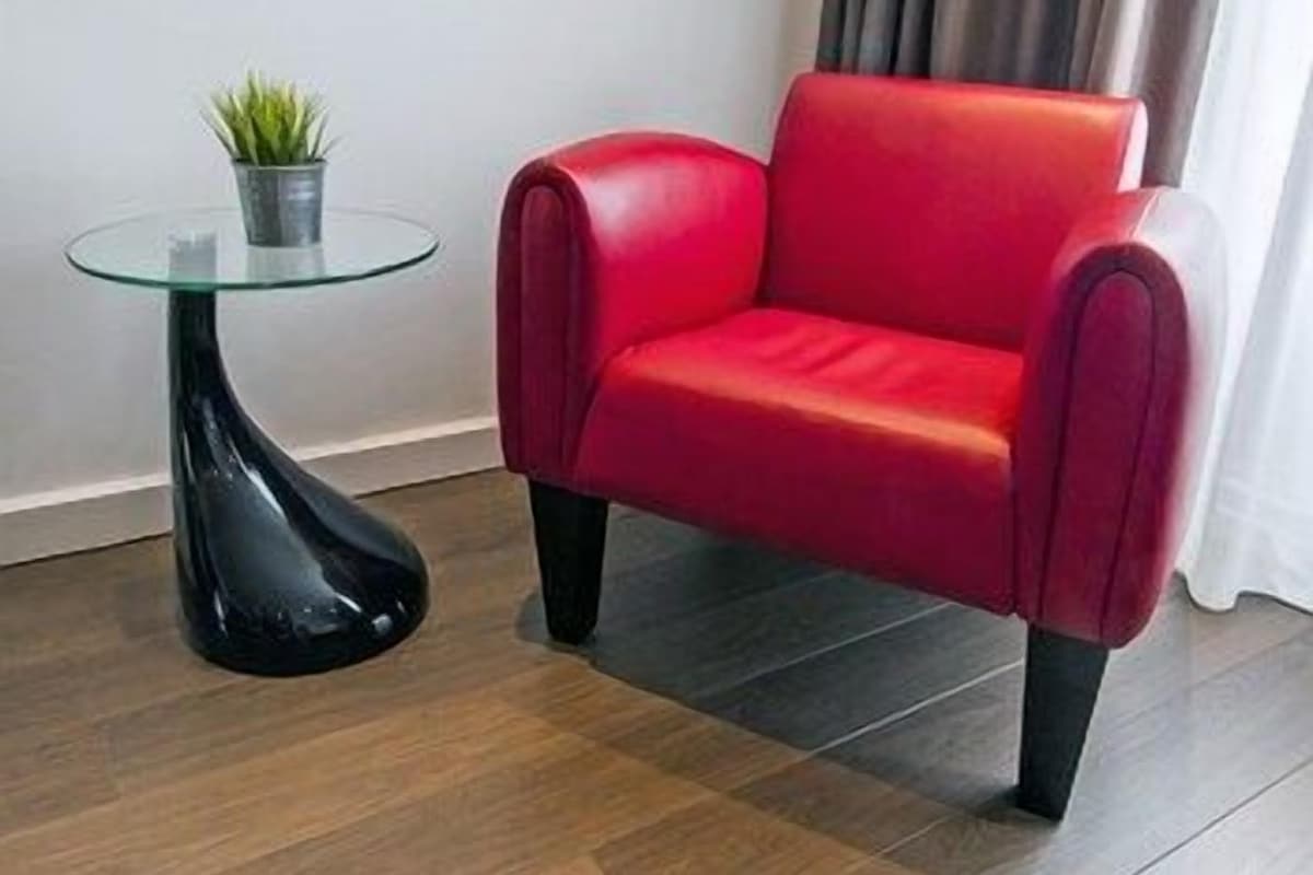 Une chaise rouge, une table en verre avec une plante, et une pièce moderne dotée d’un parquet en bois foncé.