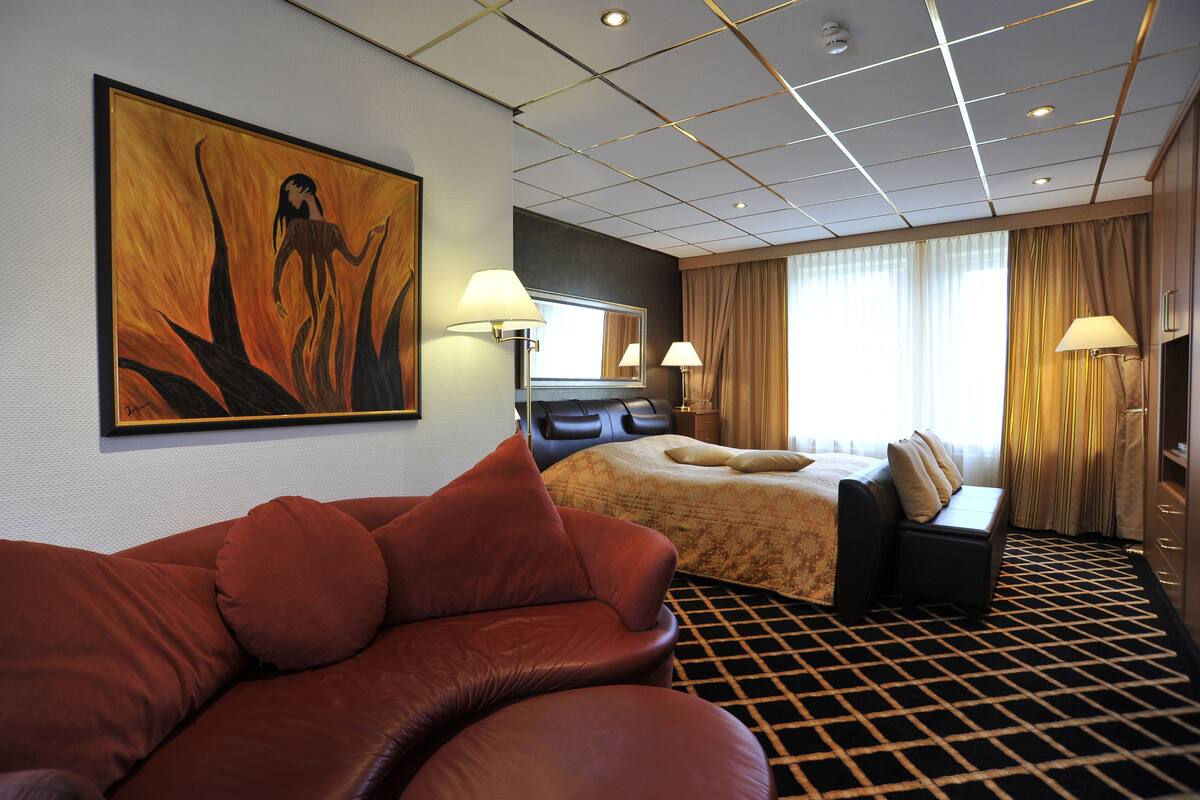 A hotel room with a large bed, a sofa, a painting on the wall, and a view of the outdoors.