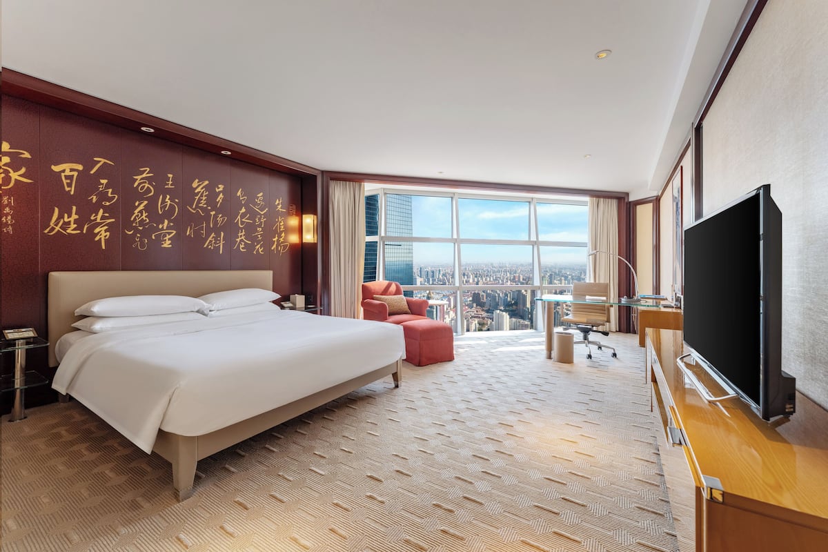 A hotel room with a large bed, a TV, a desk, and a view of the city.