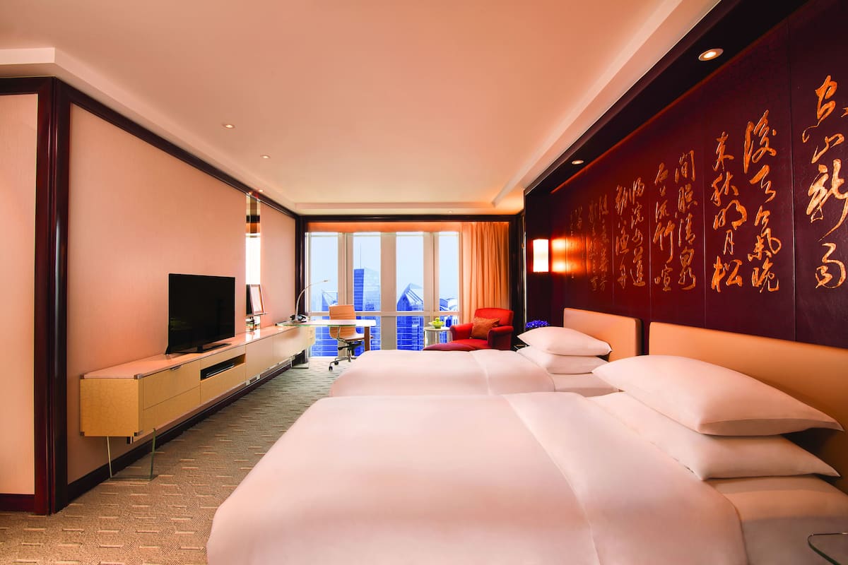 A hotel room with a large bed, a desk with a television, and a city view through the windows.