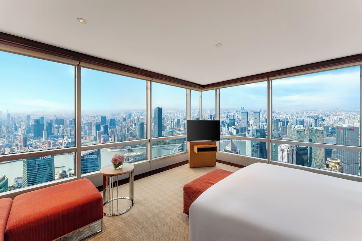A high-rise hotel room with a large window, a bed, a TV, and a small table with a vase.