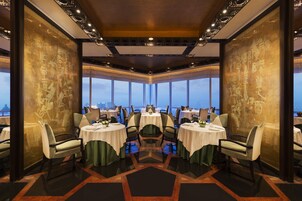 A restaurant with round tables, chairs, and a view of the cityscape through large windows.