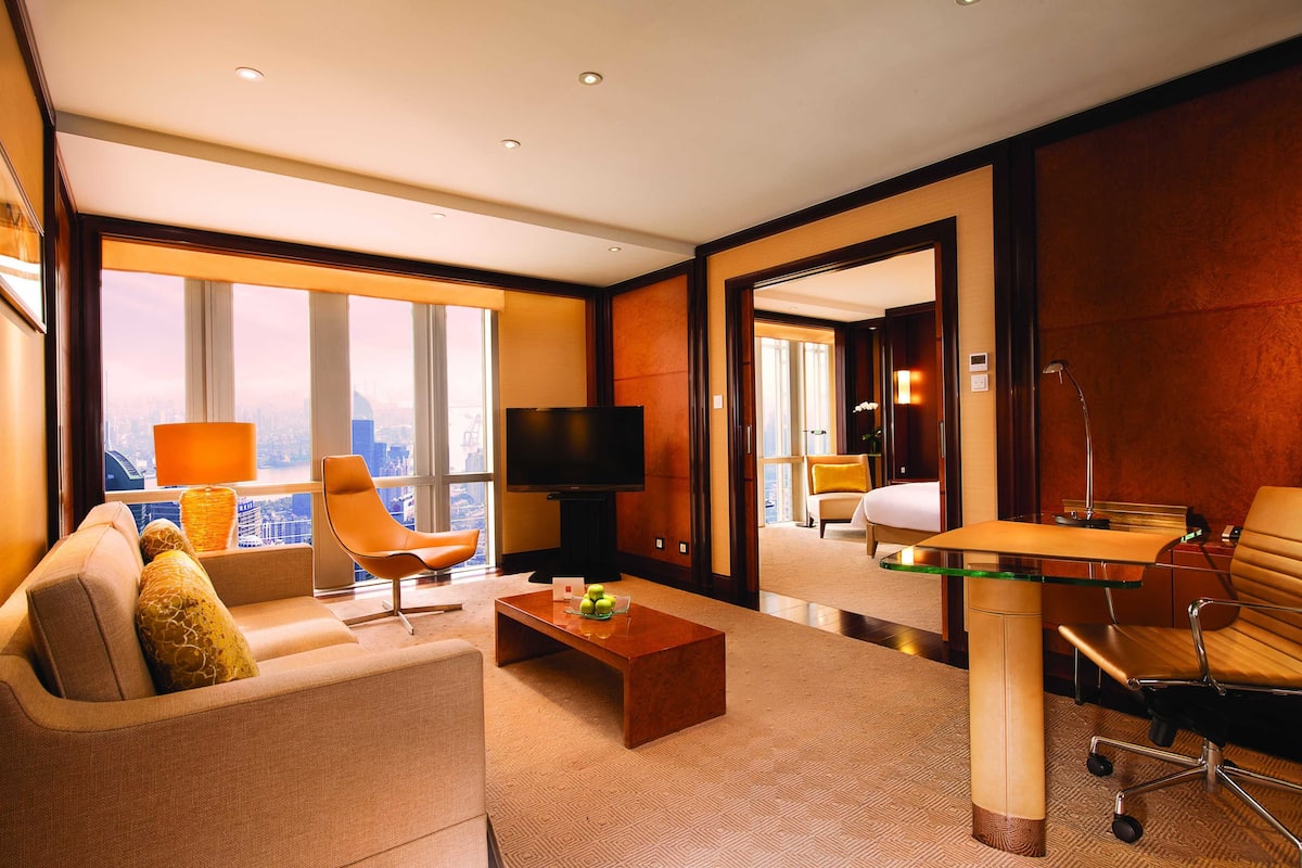 A modern hotel room with a sofa, a coffee table, a TV, and a glass-top desk.