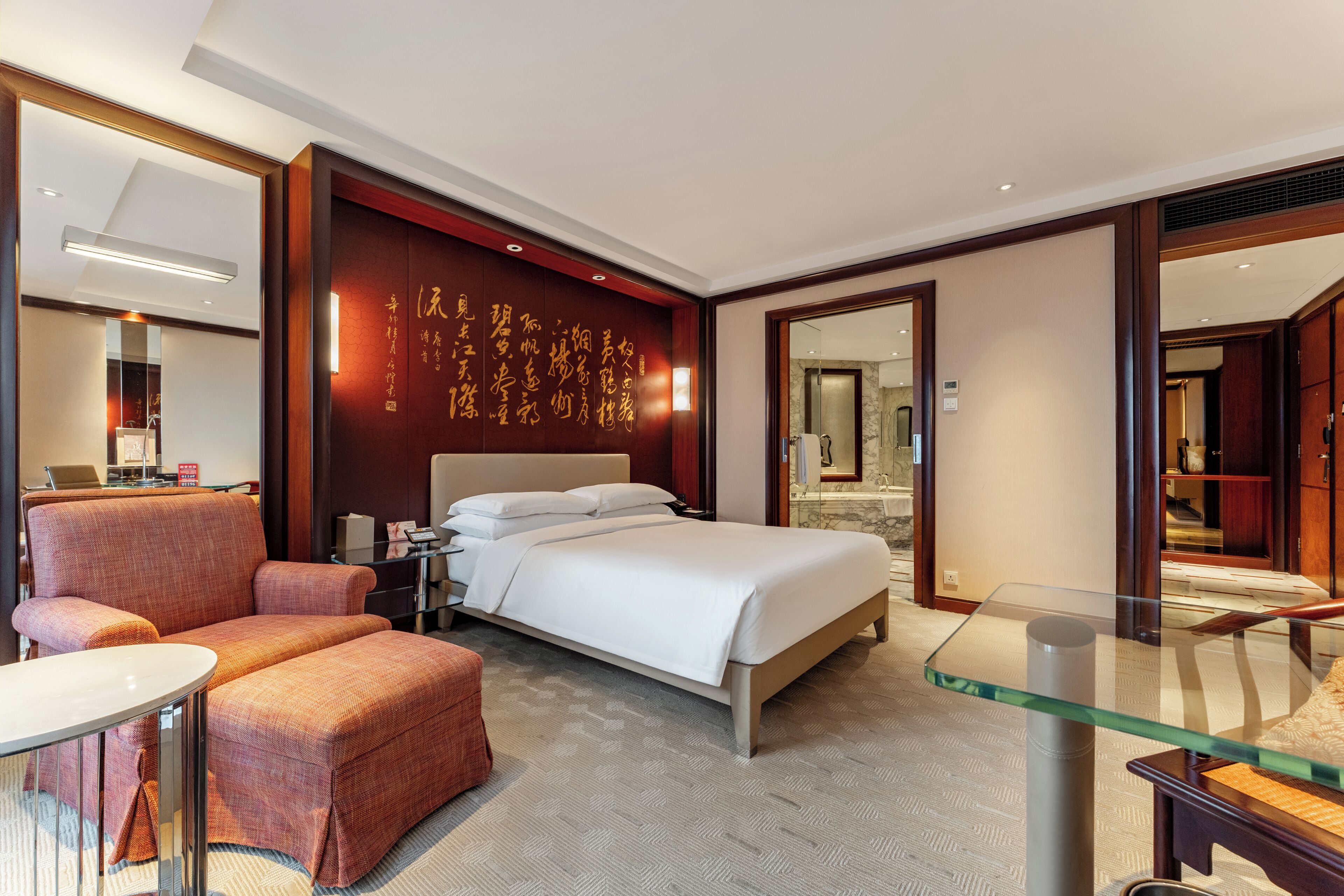 Habitación de hotel moderna con una cama grande, zona de estar, una mesita de cristal y una pared decorativa con caligrafía.