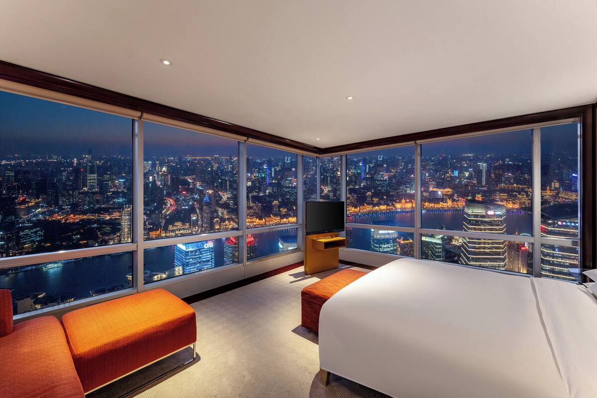 A high-rise hotel room with a city view, a bed, a TV, and a seating area.