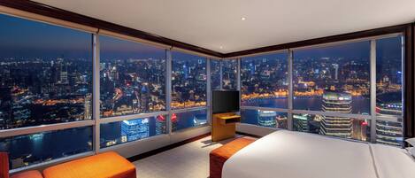 Habitación de hotel en un rascacielos con vista a la ciudad, una cama, un televisor y una zona de estar.