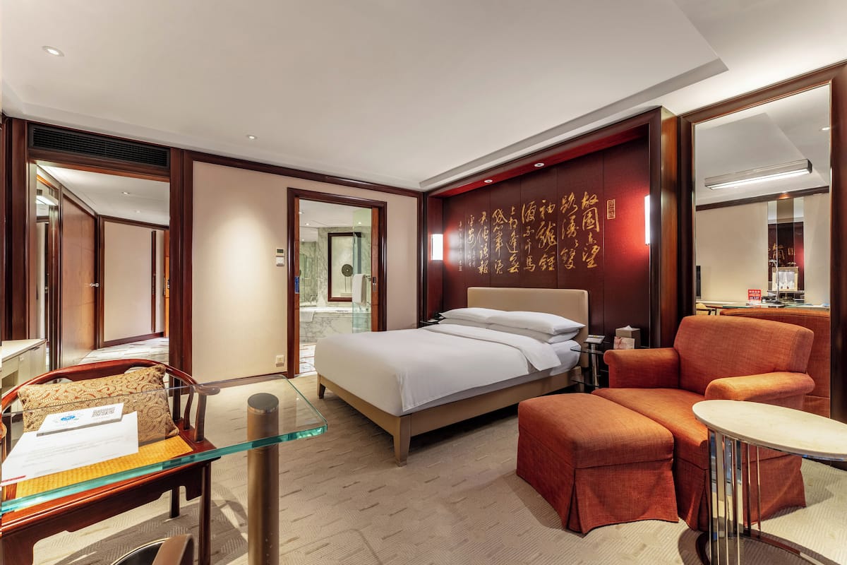 A hotel room with a bed, a seating area, a glass table, and a mirror.
