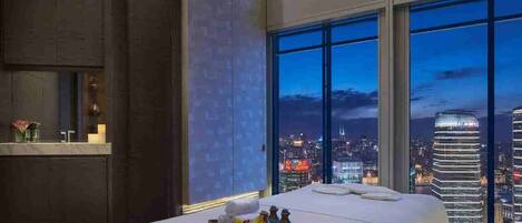 A modern hotel room with a large bed, a city view, and a small table with decorative items.