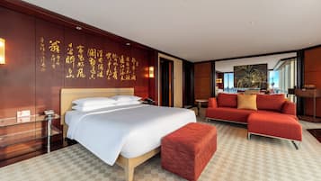 A hotel room with a large bed, a red sofa, a glass side table, and a wall with calligraphy.
