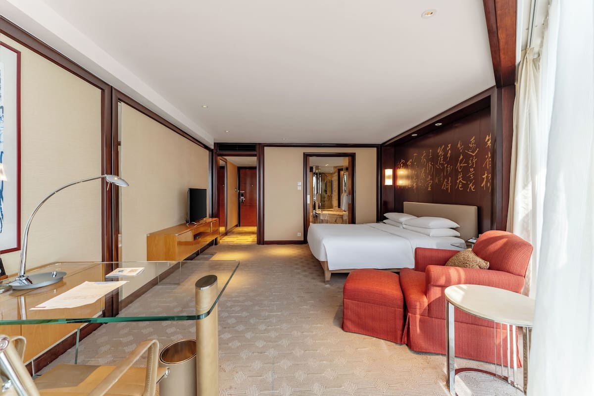 A hotel room with a bed, a desk with a computer, a chair, a sofa, and a small table.