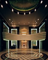 A spacious lobby with a central chandelier, a circular patterned floor, and a high ceiling with recessed lighting.
