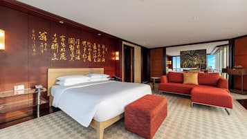 Een hotelkamer met een groot bed, een rode bank, een glazen bijzettafeltje en een rode poef. Er is een muur met Chinese karakters en een schilderij aan de muur.