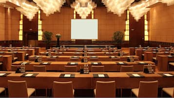 Ein großer Konferenzraum mit Tischen und Stühlen, einer großen Leinwand an der Vorderseite und Kronleuchtern.